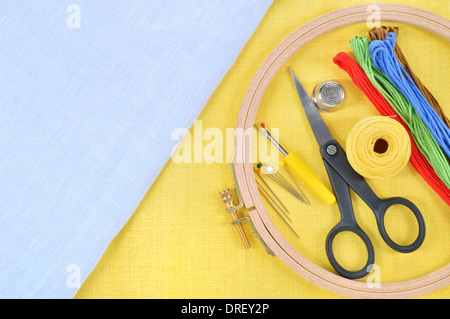 Embroidery and cross stitch accessories on yellow and light blue linen fabric. Embroidery hoop, scissors, thread, needles, thimb Stock Photo