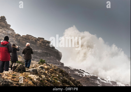 Tourists watch as very large waves crash onto rocks at Sennen Cove in Cornwall. Stock Photo