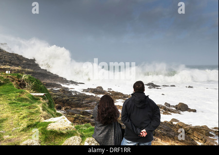 Tourists watch as very large waves crash onto rocks at Sennen Cove in Cornwall. Stock Photo