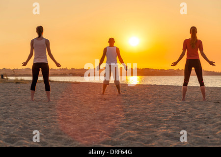 People practising yoga on beach, doing sun salutation Stock Photo