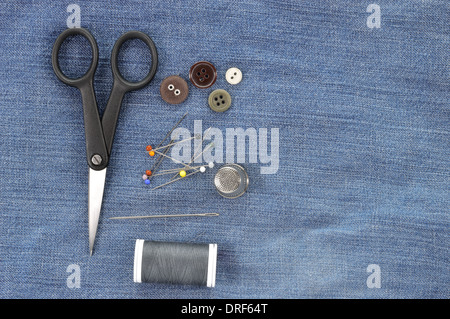Sewing kit on jeans background. Needle, pins, buttons, thread, thimble and scissors - repair set. Copy space. Stock Photo