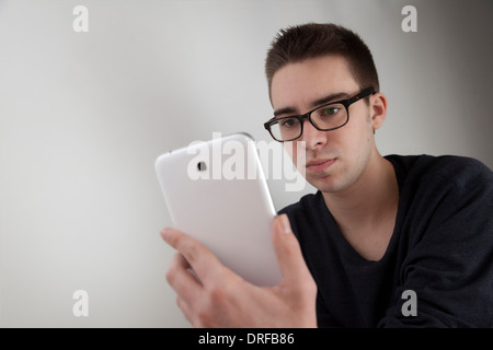 Good looking young man wearing glasses, holding a white digital tablet. Landscape shape, with copy space. young man using digita Stock Photo