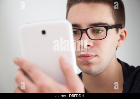 Good looking young man wearing glasses, holding a white digital tablet. Serious expression. Stock Photo