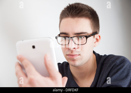 Good looking young man wearing glasses, holding a white digital tablet. Serious expression. Stock Photo