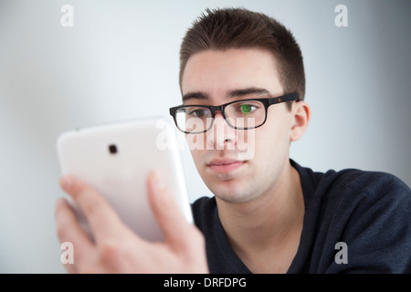Good looking young man wearing glasses, slight reflection. Holding a white digital tablet. Serious expression. Stock Photo