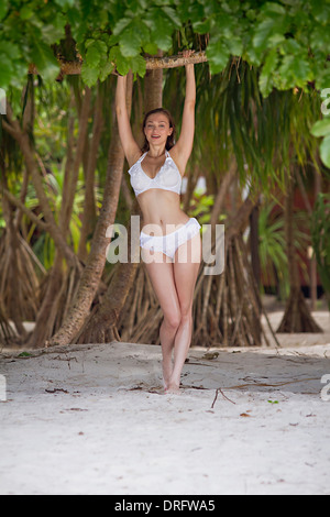 Young woman in bikini standing on beach, arms raised. Lankayan Island, Borneo, Malaysia