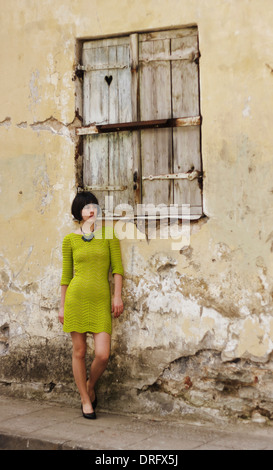Young adult woman lean on an old building wall with a closed shutter. Small heart in shutter. Stock Photo
