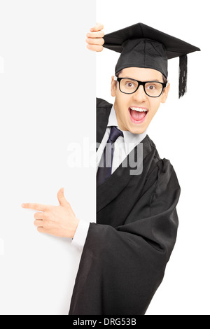 Male graduate student peeking from behind a blank panel and pointing with finger Stock Photo