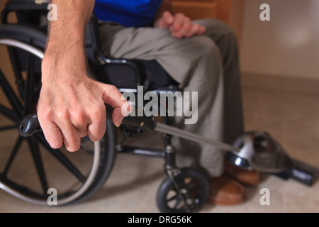 Man with Friedreich's Ataxia and deformed hands vacuuming his house from his wheelchair Stock Photo