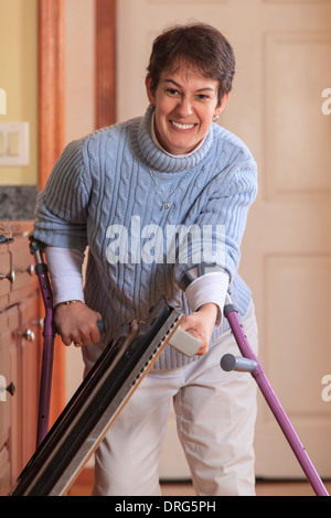 Woman with Cerebral Palsy using crutches and opening her dishwasher in her kitchen Stock Photo