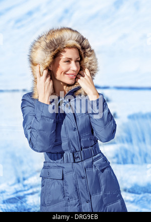 Portrait of cute woman wearing warm coat with hood with fur, having fun in winter park, wintertime fashionable style Stock Photo