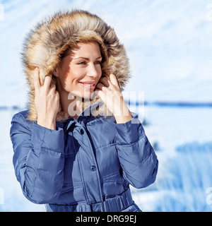 Closeup portrait of cute woman wearing warm coat with hood with fur, having fun in winter park, wintertime fashionable style Stock Photo