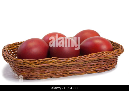 Three Easter eggs, painted in red, are beautifully decorated with wicker basket. Presented on a white background. Stock Photo