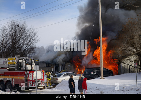 Residents outside in night clothes in winter with snow while house goes up in flames with firefighters spraying water on fire in Ottawa Stock Photo