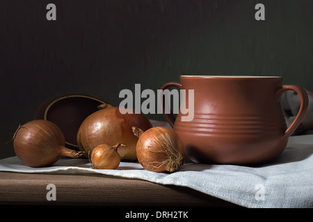 Still-life with a clay pot and onions on a wooden board Stock Photo