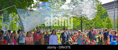 Families enjoying a demonstration of big bubble creations using a large net and cord wand on two poles Stock Photo