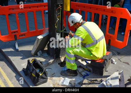 Close up of electrician engineer working on wiring & electrical cables at base of street lighting column everyday street scene London England UK Stock Photo