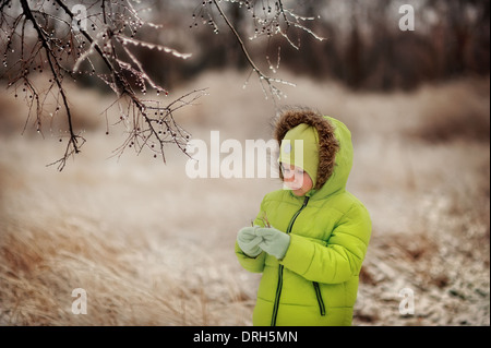 boy in a green suit walks in the park in winter with frozen trees and grass Stock Photo