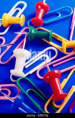 Colorful thumbtacks and paperclips on blue background, office supplies conceptual still life Stock Photo