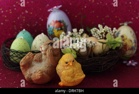 A ceramic bunny laying down next to a ceramic baby chicken in front of a nest with eggs in it. Stock Photo