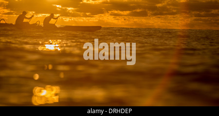 silhouette of two one man canoes paddling off Waikiki Beach at sunset. Stock Photo