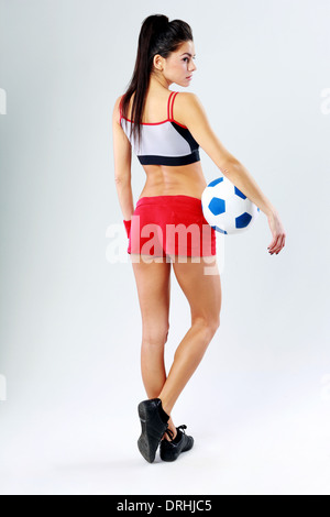 Back view portrait of a young beautiful sport woman standing with soccer ball and looking away on gray background Stock Photo