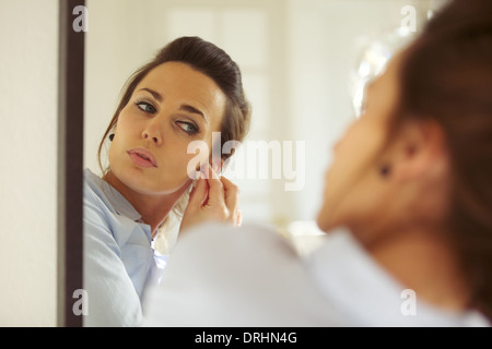 Attractive young woman putting on her earrings while looking at the mirror. Caucasian businesswoman getting dressed.