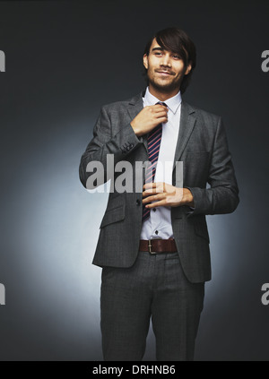 Image of confident young man in business suit looking away and adjusting his necktie. Asian male model against black background. Stock Photo