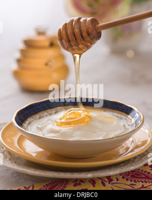 Honey drizzling over yogurt with a honey pot in the background Stock Photo