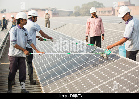 Workers washing dust off soalr panels at a 1 MW solar power station run by Tata power on the roof of an electricity company in Delhi, India, to make them more efficient. Stock Photo