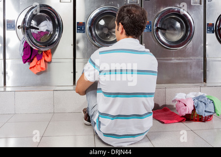 Man Sitting In Front Of Washing Machines Stock Photo