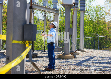 Power engineer using his cell phone at high voltage power distribution station, Braintree, Massachusetts, USA Stock Photo