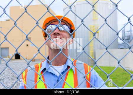 Engineer at electric power plant inside secured fence looking at power plant buildings Stock Photo