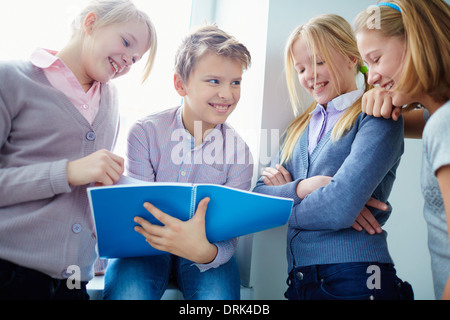 Portrait of three happy schoolgirls looking at notes in exercise book held by schoolboy Stock Photo