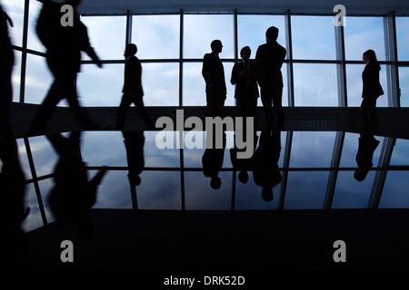 Three white collar workers communicating in office against window with several business partners walking around Stock Photo