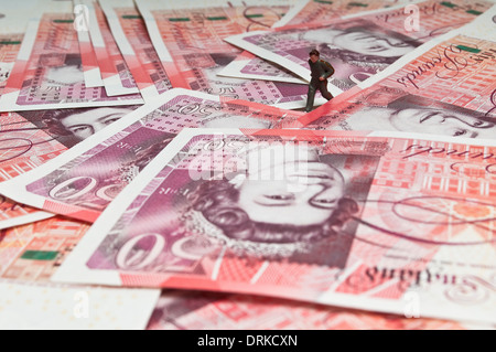 Miniature figure running over a pile of fifty pound banknotes Stock Photo