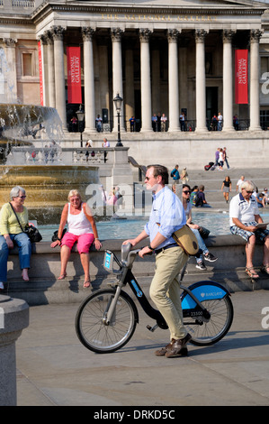 London, England, UK. Man pushing 'Boris Bike' / Barclay's rental cycle in Trafalgar Square Stock Photo