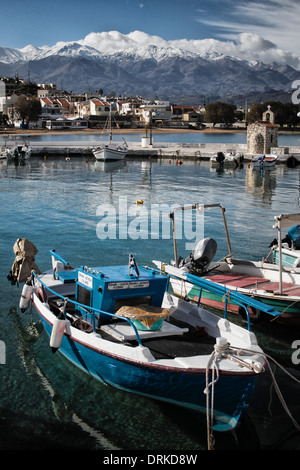 Winter in Crete: fishermen's boats tied up in the marina of Kalyves with the snow-covered White Mountains in the background. Stock Photo