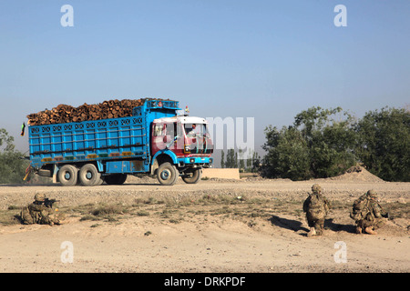 US soldiers provide security at their patrol base as a truck carrying logs passes along the road June 14, 2012 outside the village of Tatanak in Paktya province, Afghanistan. Stock Photo