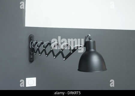 Black adjustable lamp mounted on grey wall. Stock Photo
