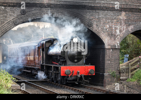 Steam train passing under brick bridge Stock Photo