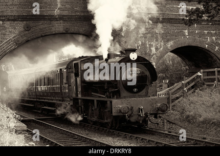 Steam train passing under brick bridge Stock Photo