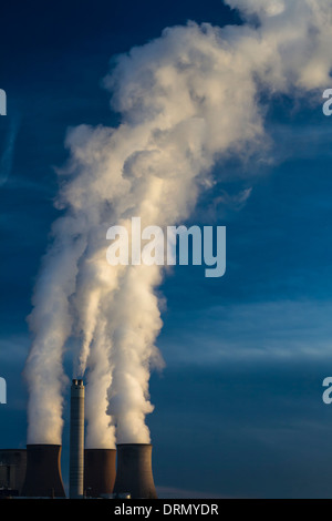 A dramatic view of the cooling towers of a power station at full power, billowing tall plumes of smoke into a clear blue sky. Stock Photo