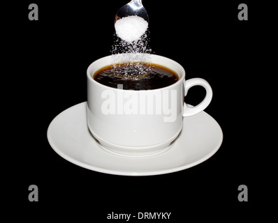 Sugar is poured from a spoon into a cup of coffee isolated on a black background Stock Photo