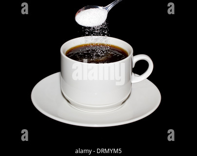 Sugar is poured from a spoon into a cup of coffee isolated on a black background Stock Photo