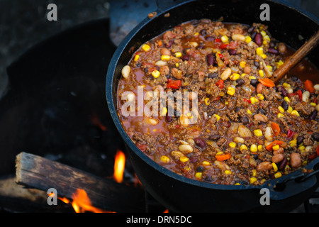 Large cast iron pot of spicy chili cooking over a campfire Stock Photo