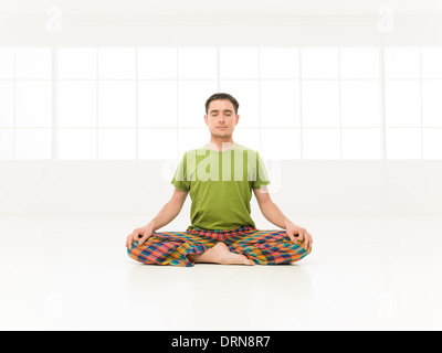 Young man doing yoga in white window studio lotus position Stock Photo