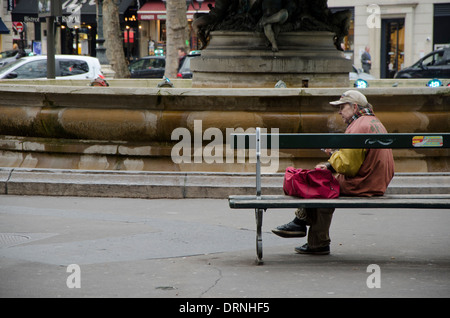 Older homeless woman smoking a cigarette in front of a fountain in Paris, France. Stock Photo