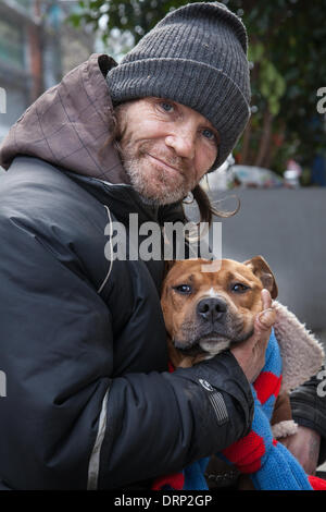 Homelessness in Manchester, UK.   UK Weather.  Mr John Stokes, 47 with his dog, a homeless man on the streets of Manchester. There is an increased threat to Homeless and those sleeping rough as the cold snap begins. Here his dog is wrapped in sheepskin coat with a blue and red scarf as protection against the colder weather forecast over the weekend. Stock Photo