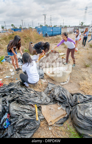 A team of Asian American and Hispanic teen girls remove trash from a blighted vacant lot in a slum of Stanton, California. Note dumpster in background. Stock Photo